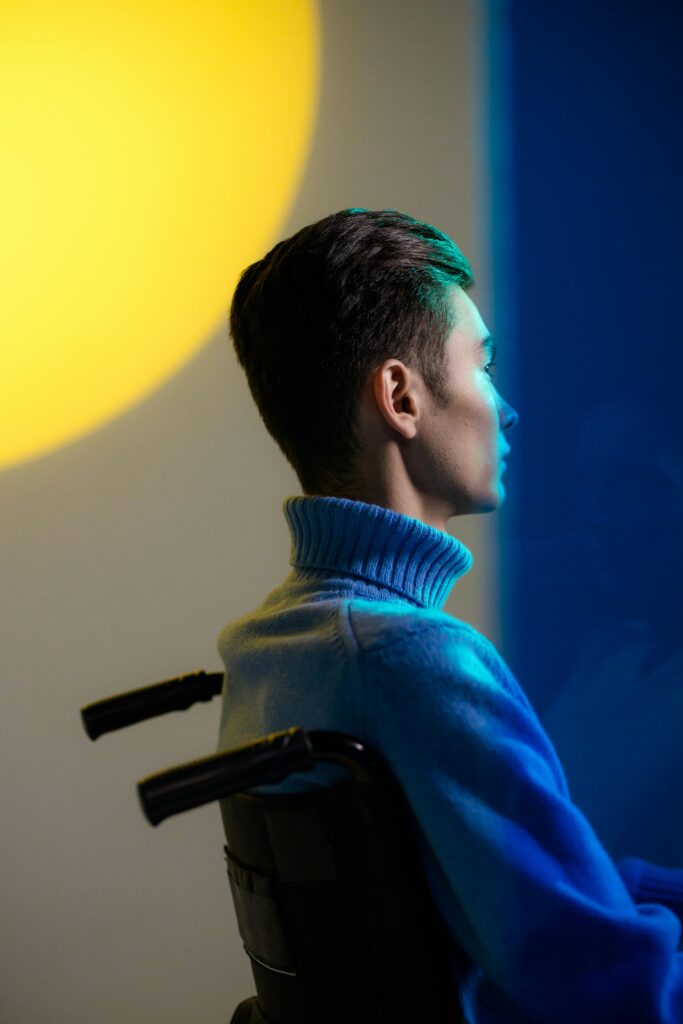 Side view of a young man in a wheelchair, highlighted by dramatic light and shadow.
